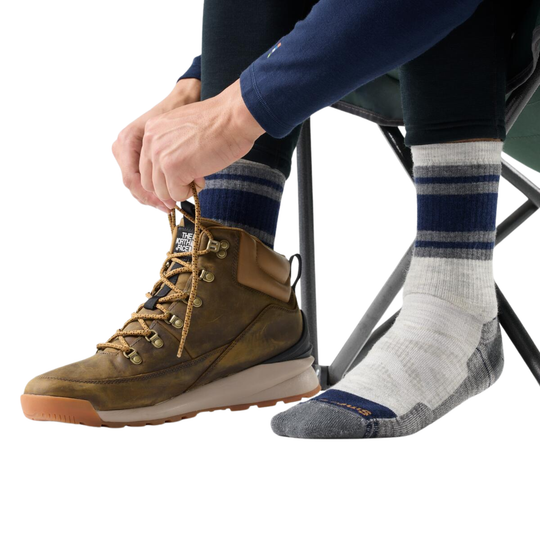 Person putting on a hiking boot wearing White, Blue and grey socks while sitting on a chair