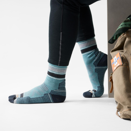 Person wearing blue striped socks with black accents, standing next to a beige backpack.