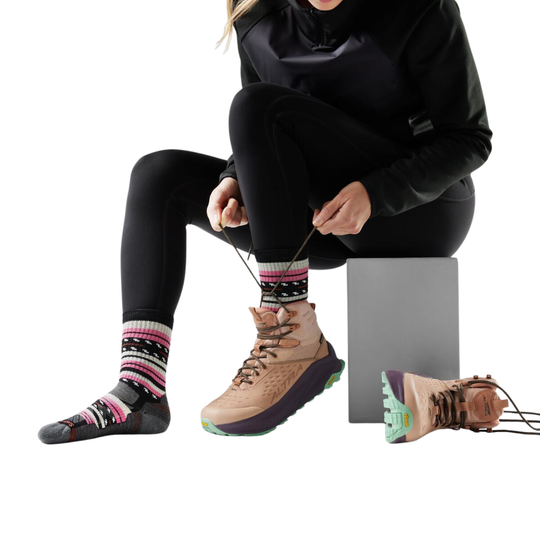 Person sitting on a block wearing black leggings, colorful socks, and brown hiking boots.