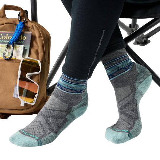 Person wearing gray hiking socks with a brown backpack, sunglasses, and map on a white background