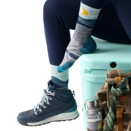 Person wearing blue hiking boots and patterned socks with a teal suitcase and backpack on a white background.