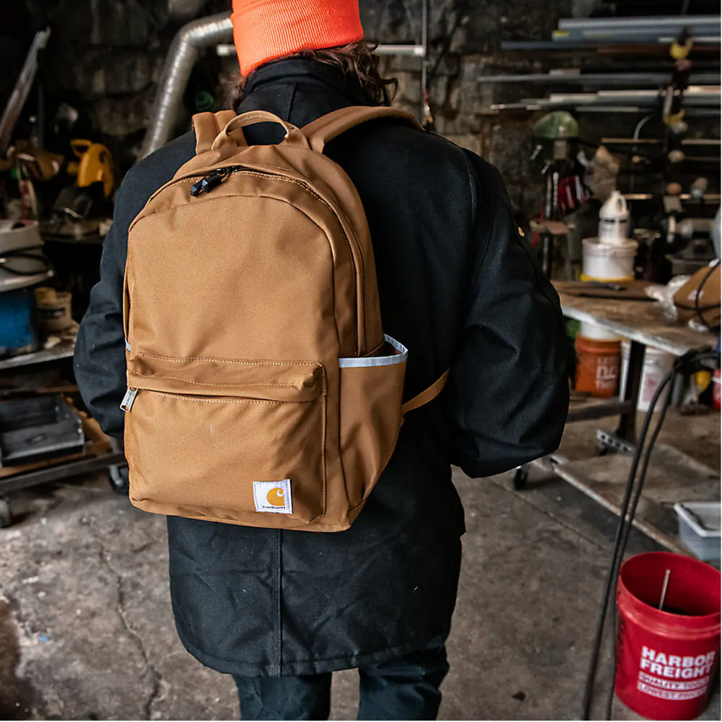 Person wearing a brown backpack with a visible brand logo in a workshop setting.