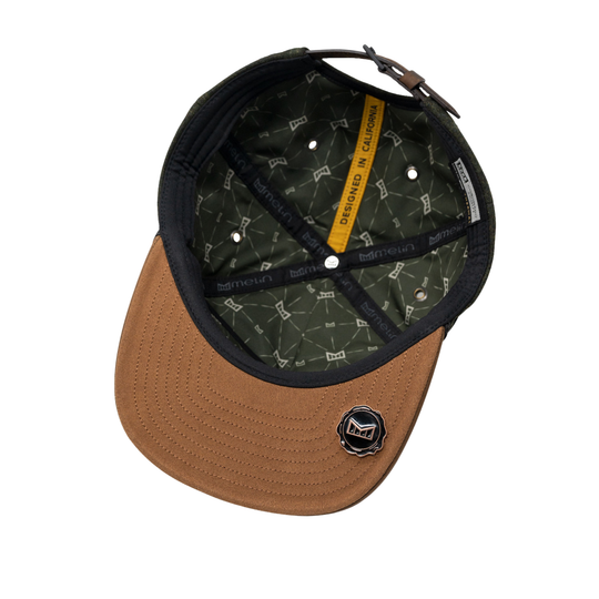 A brown and black baseball cap shown from a top-down angle, revealing a dark green patterned interior with a yellow 'DESIGNED IN California' tab and a small circular black and white logo on the brim.