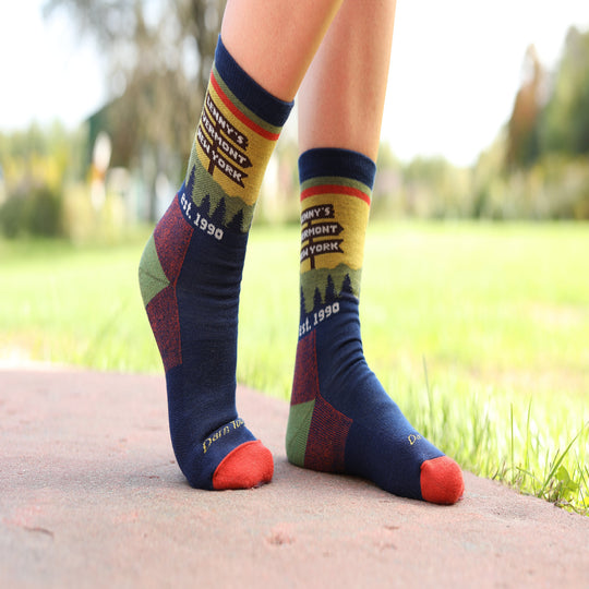 A person wearing colorful crew socks with a New York-themed graphic design, standing on a concrete path with a blurred green grassy background.