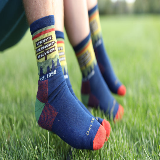 Close-up of a person's legs sitting on green grass, wearing navy blue crew socks with colorful graphics and text.