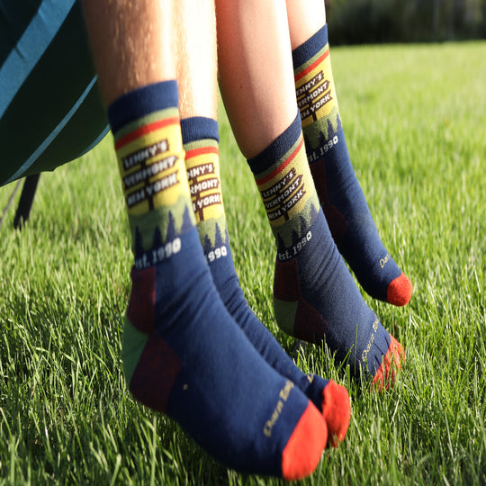 Close-up of a person's legs sitting on green grass, wearing navy blue crew socks with colorful graphics and text.
