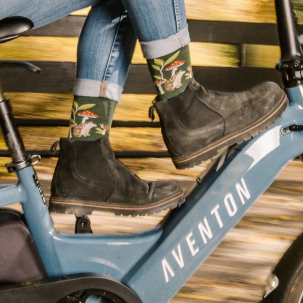 Person wearing floral-patterned socks and dark boots on a blue Aventon bike.