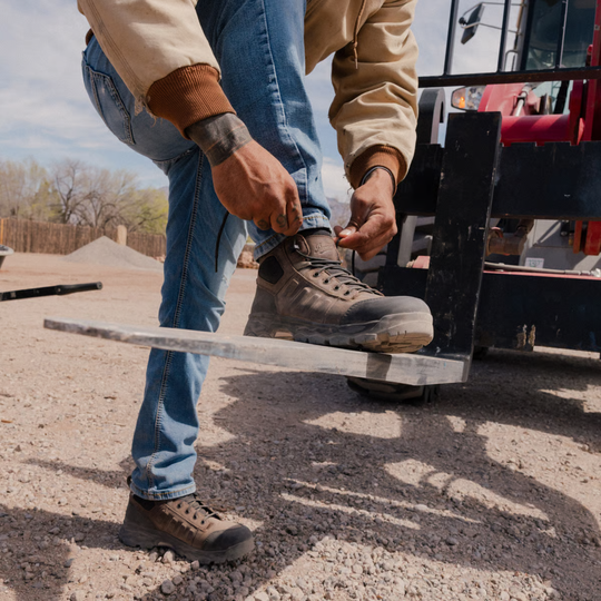 dirt gravel with red machinery in background. Man wearing wheat ridge work boots
