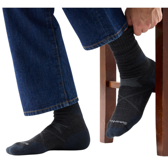 Person wearing charcoal socks with blue jeans sitting on a wooden stool.