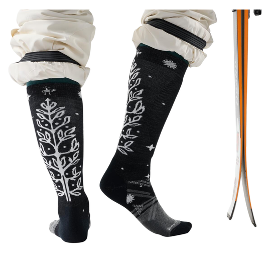 Black knee-high socks with white patterns worn by a person, with a ski in the background.