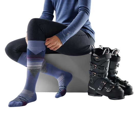 Person wearing blue patterned socks and black ski boots on a white background