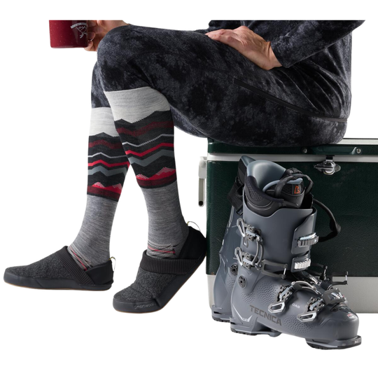 Person sitting with striped socks and gray ski boots on a white background