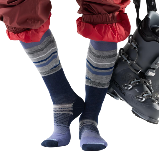 Person wearing blue striped socks with red pants and a black ski boot on a white background