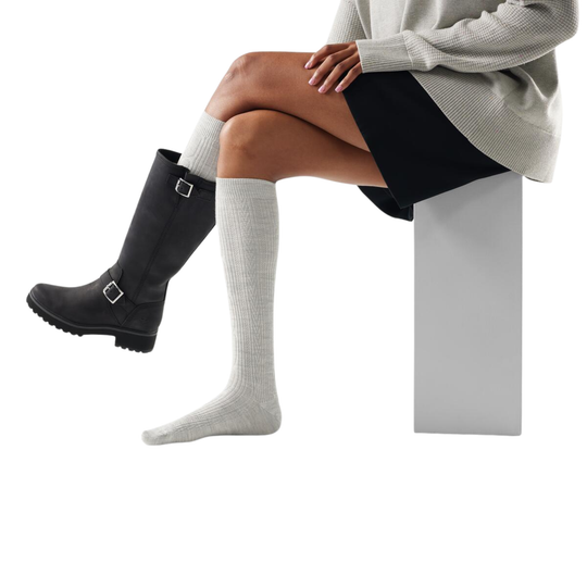 Person wearing black rain boots and ash colored knee-high socks on a white background
