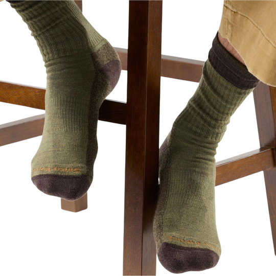 Green socks with brown toes and cuffs worn by a person sitting on a wooden chair.