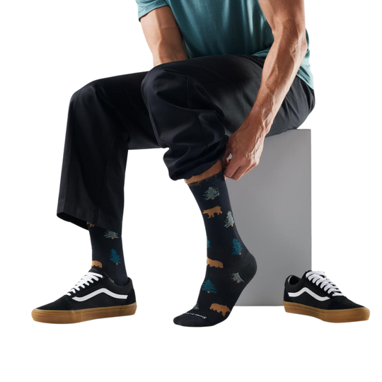 Person wearing black socks with bear designs and black sneakers on a white background