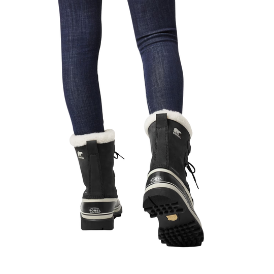 Black winter boots with white fur lining worn with blue jeans on a white background