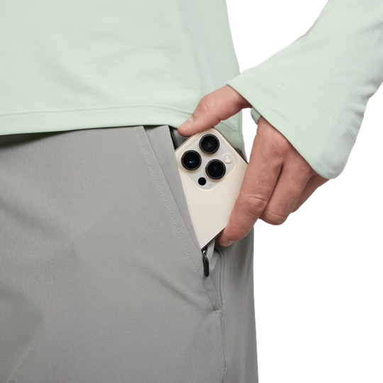 Person holding a phone in a pocket with a light green shirt and gray pants.