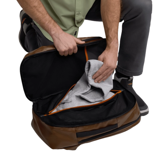 Person opening a brown and black duffel bag with a gray towel inside on a white background