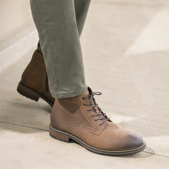 Brown leather boots worn with green pants on a neutral background