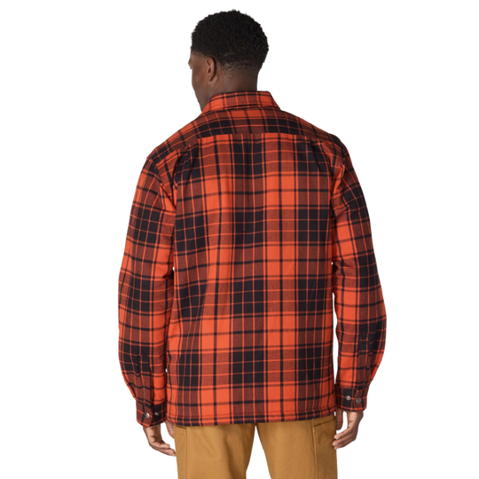 A man viewed from the back wearing a red and black plaid flannel shirt and tan pants, set against a plain white background.