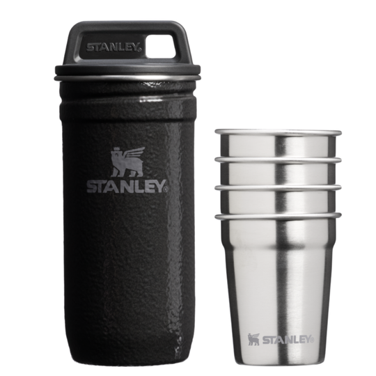 A black Stanley insulated bottle with a matching black lid is shown next to a stack of four stainless steel cups on a plain white background.