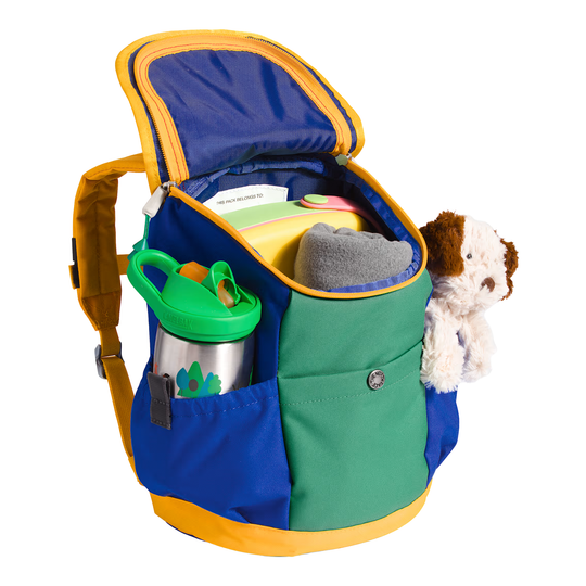 A colorful dog-shaped backpack shown open, filled with storage compartments, a green water bottle, and a plush dog toy, on a white background.