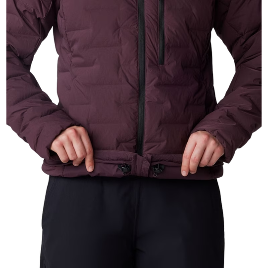 A close-up of a person wearing a quilted puffer jacket in a dark plum-burgundy color, with black pants visible below against a plain white background.