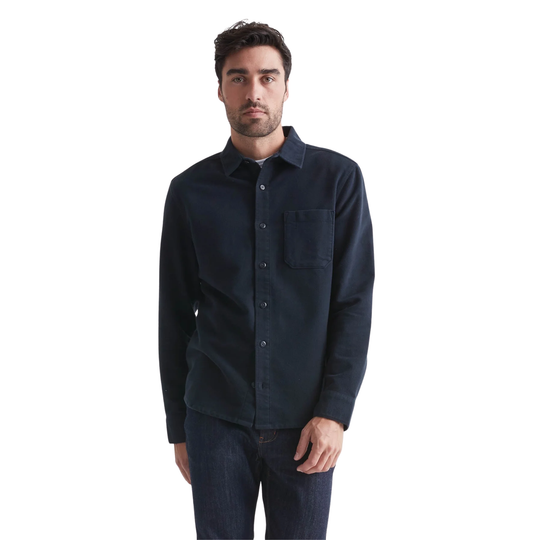 A man wearing a dark navy long-sleeve button-up shirt with a chest pocket, paired with dark jeans, photographed against a solid white background.