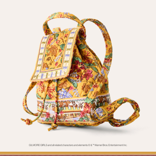 A small drawstring backpack in a vintage-style floral print with yellow, orange, red, green, and blue patterns, shown on a light beige background. The print features a mix of floral motifs and geometric borders.