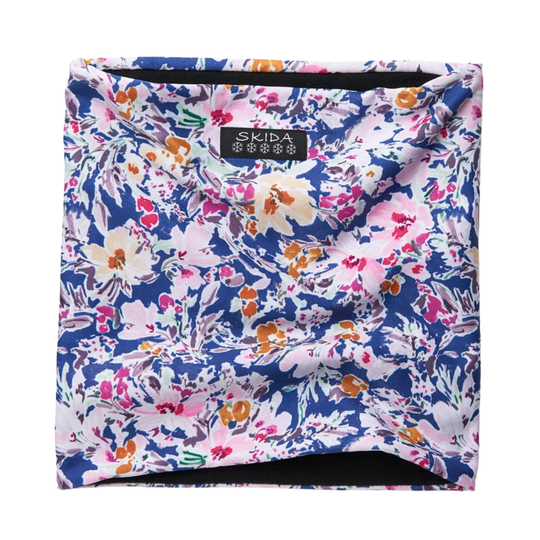 A square neck gaiter or face covering by Skida, featuring a vibrant floral print on a navy blue background with pink, white, orange, and purple blossoms. The brand label 'SKIDA' is visible at the top center.