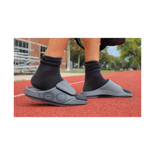 Gray slide sandals with contoured footbeds and strap logos worn with black socks on a track