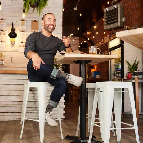 Man seated at a cafe table wearing cuffed dark jeans, gray socks, and white high-top sneakers