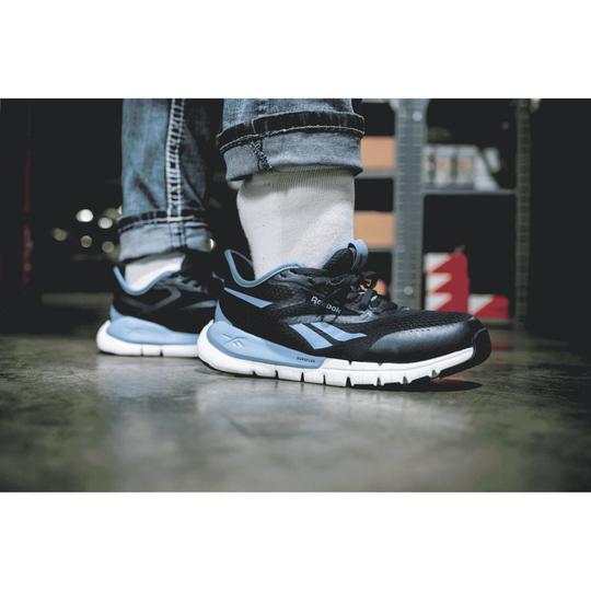 Black and blue running shoes worn with jeans on a blurred background