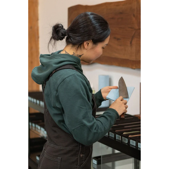 Person in green hoodie and apron sharpening a knife with a stone