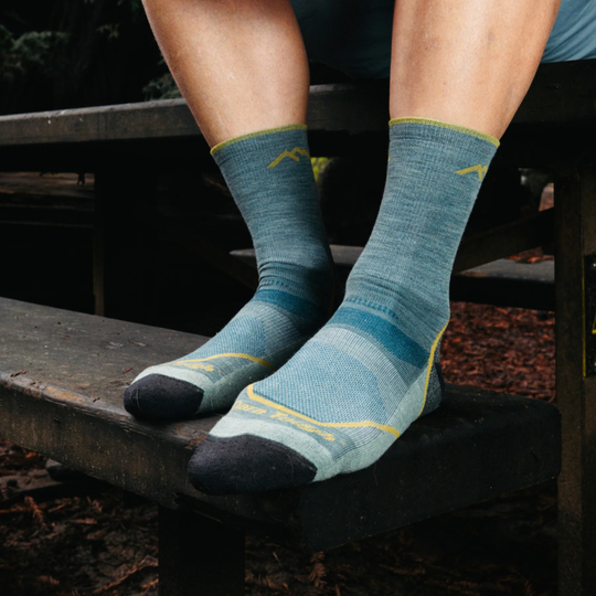 Person wearing blue patterned socks with yellow accents on a wooden bench.