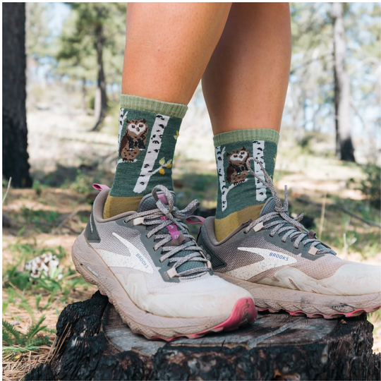 Person wearing socks with owl design and running shoes in a forest setting