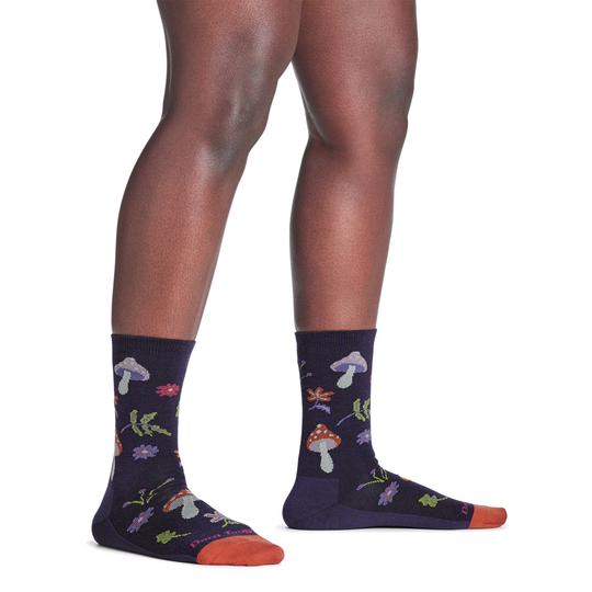 Black crew socks with mushroom and flower pattern, orange toes, worn on a model's legs