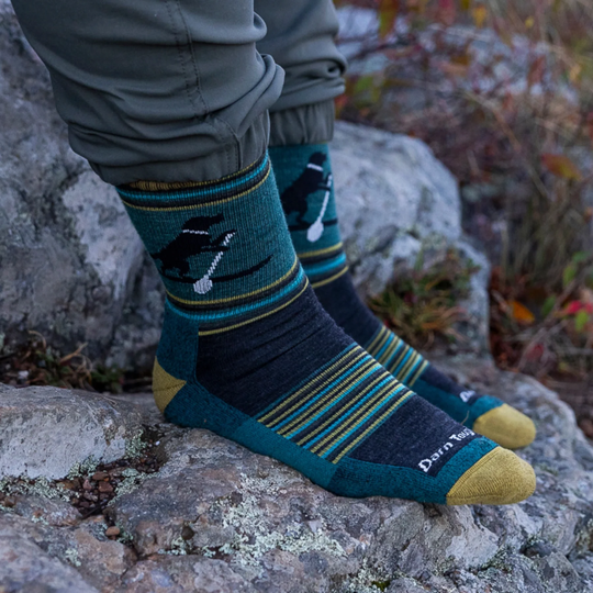 Person wearing blue and green patterned socks with a gold accent on a rocky surface.