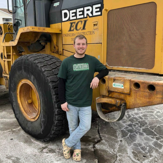 Man standing next to a large yellow construction vehicle with 'Deere' branding.