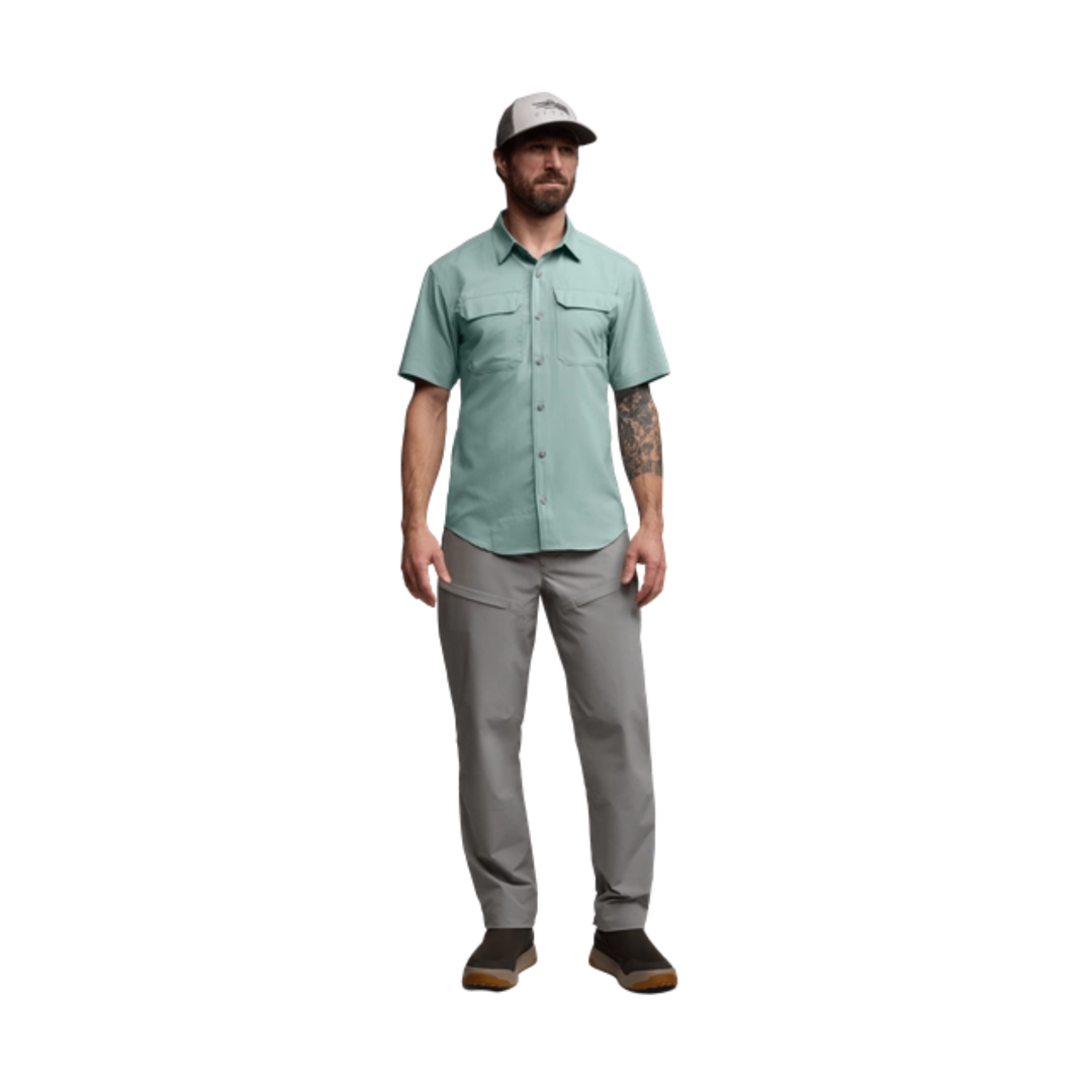 Man wearing a light green shirt and gray pants on a white background