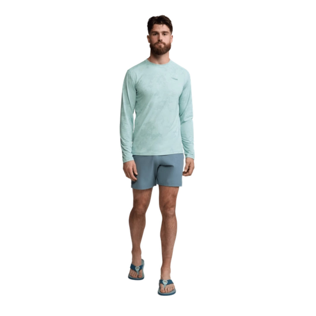 Man wearing a light blue long-sleeve shirt and gray shorts on a white background