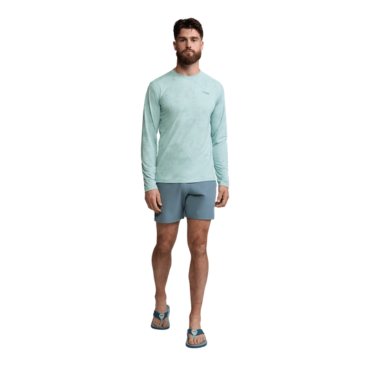 Man wearing a light blue long-sleeve shirt and gray shorts on a white background