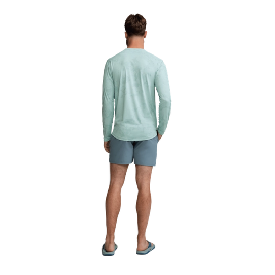 Man wearing a light green long-sleeve shirt and gray shorts on a white background