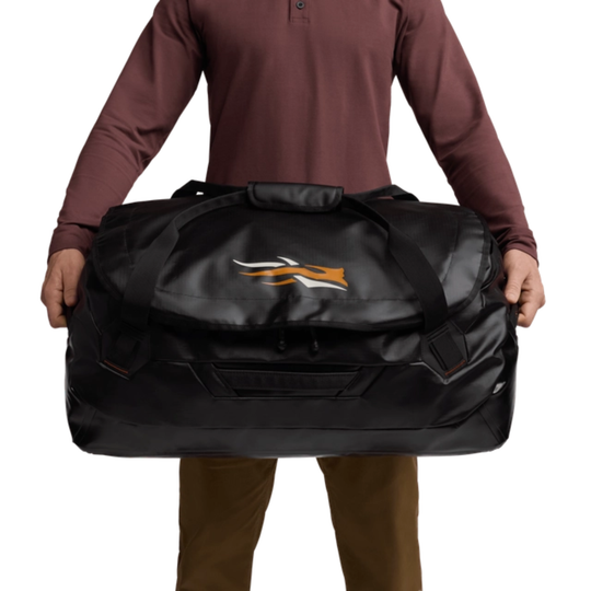 Person holding a large black duffel bag with a logo on a white background