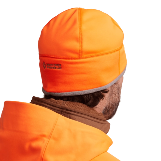 Person wearing an orange hunting cap and jacket on a white background
