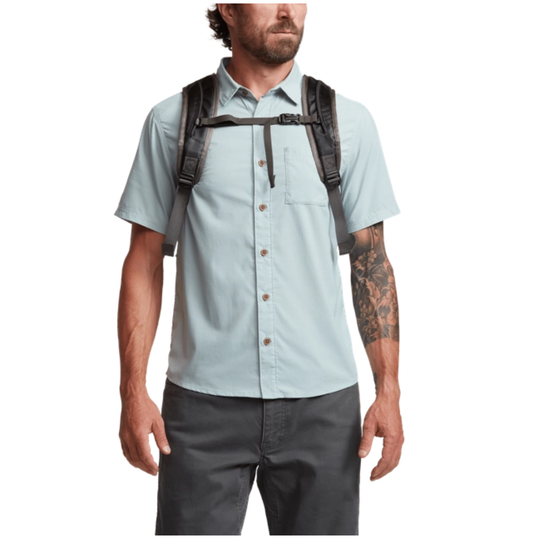 Man wearing a light blue shirt, dark pants, and a black backpack on a white background