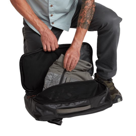 Person packing a black suitcase with clothes on a white background