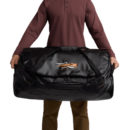 Person holding a large black duffel bag with a logo on a white background