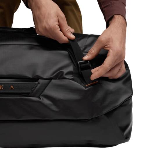 Person adjusting a black bag strap with a visible brand logo.